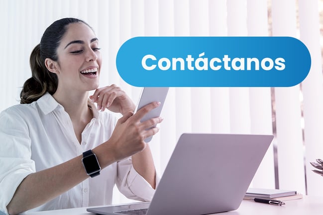 Mujer sonriente usando un smartphone en el escritorio con un portátil, junto a un gran botón azul de ‘Contáctanos’.